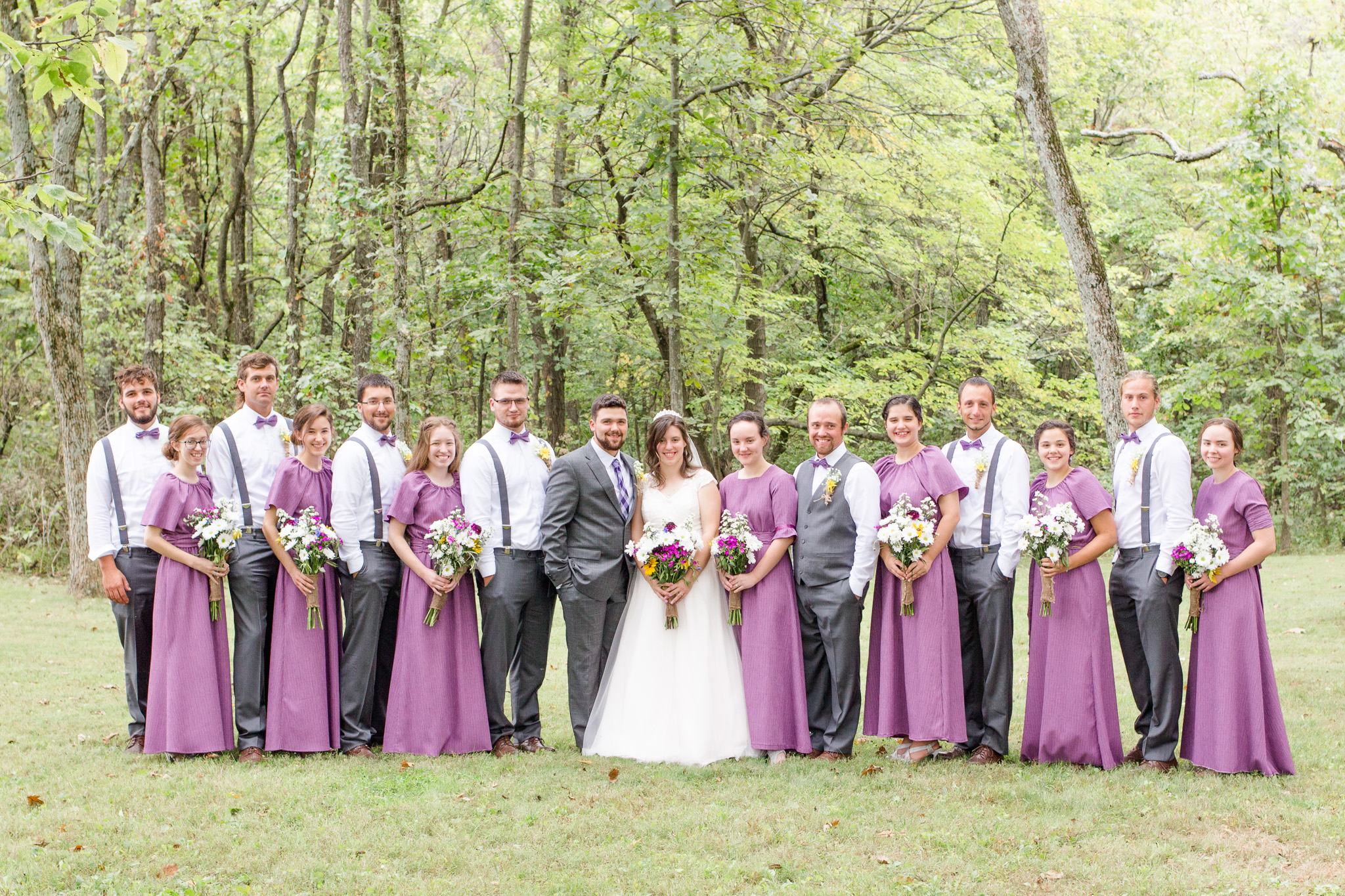 Purple bridesmaid dresses and groomsmen with gray pants and suspenders